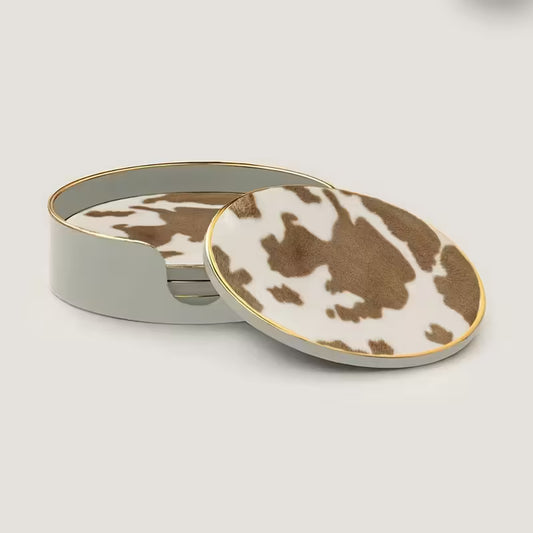 Set of cow print coasters with a matching round container on a light gray background